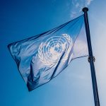UN flag waved against the sun and blue sky.