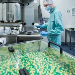 Pharmaceutical industry man worker in protective clothing operating production of tablets in sterile working conditions